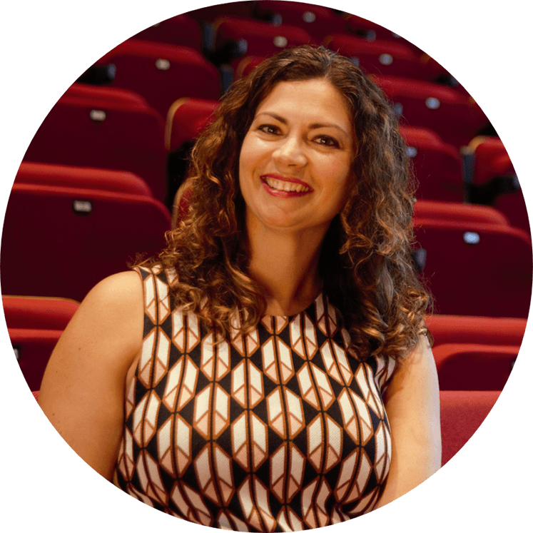 young woman, white, with curly brown hair and a beautiful smile, sitting inside a theater