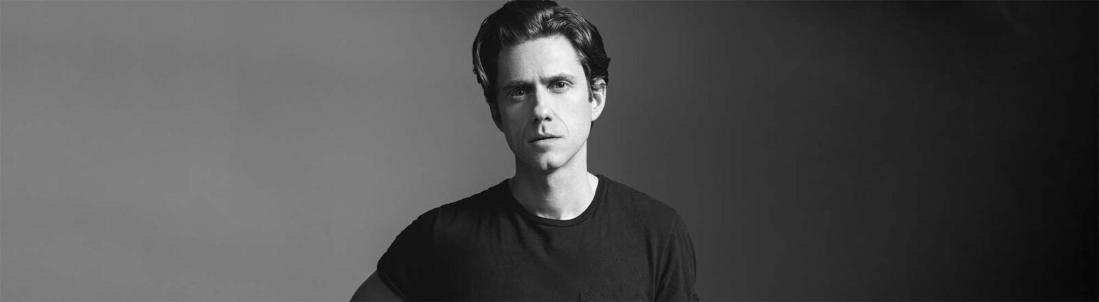 Aaron Tveit, standing up, looking serious in black and white color