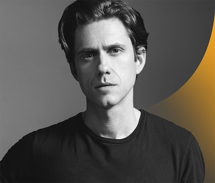 Aaron Tveit, standing up, looking serious in black and white color