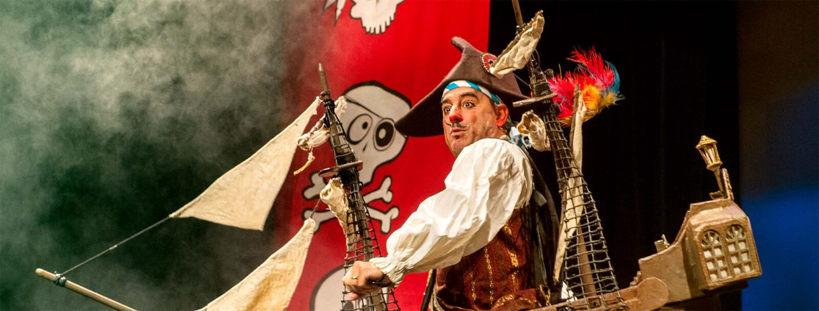 A pirate on top of a sailing ship with red banners on his back