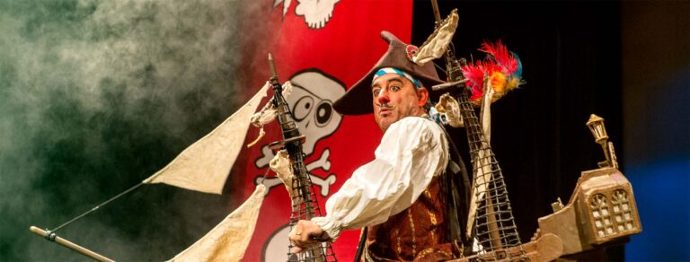 A pirate on top of a sailing ship with red banners on his back