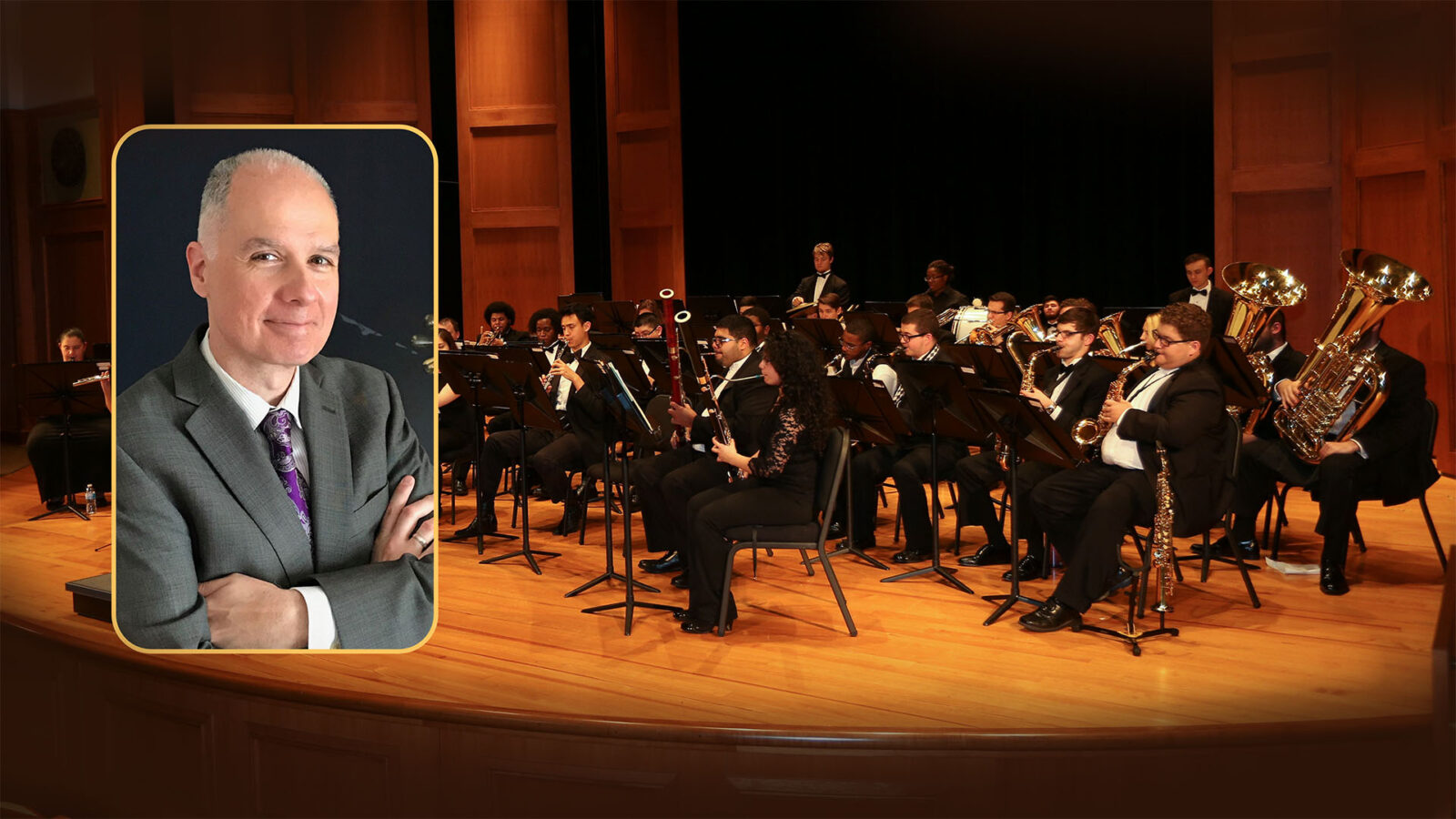 A concert band is performing on a wooden stage in a dimly lit auditorium, with a variety of instruments including brass and woodwinds. An inset portrait of a distinguished man in a suit, arms crossed, is positioned on the left.