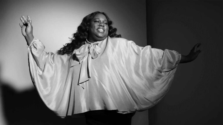 A black and white image showcases Alex, a black African woman with open arms and a flowing blouse.