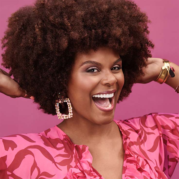 Tabitha with a big smile and afro, dressed in a pink shirt with dark pink pattern