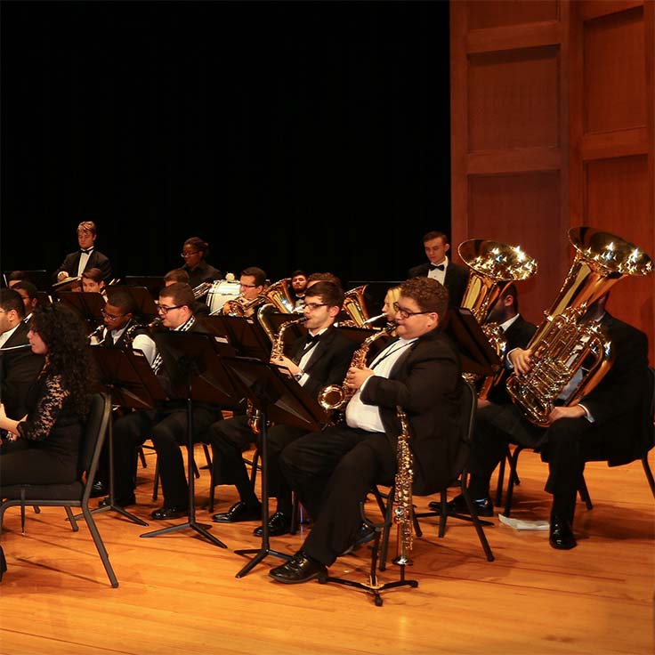 A group of students on stage dressed in black suits playing wind instruments