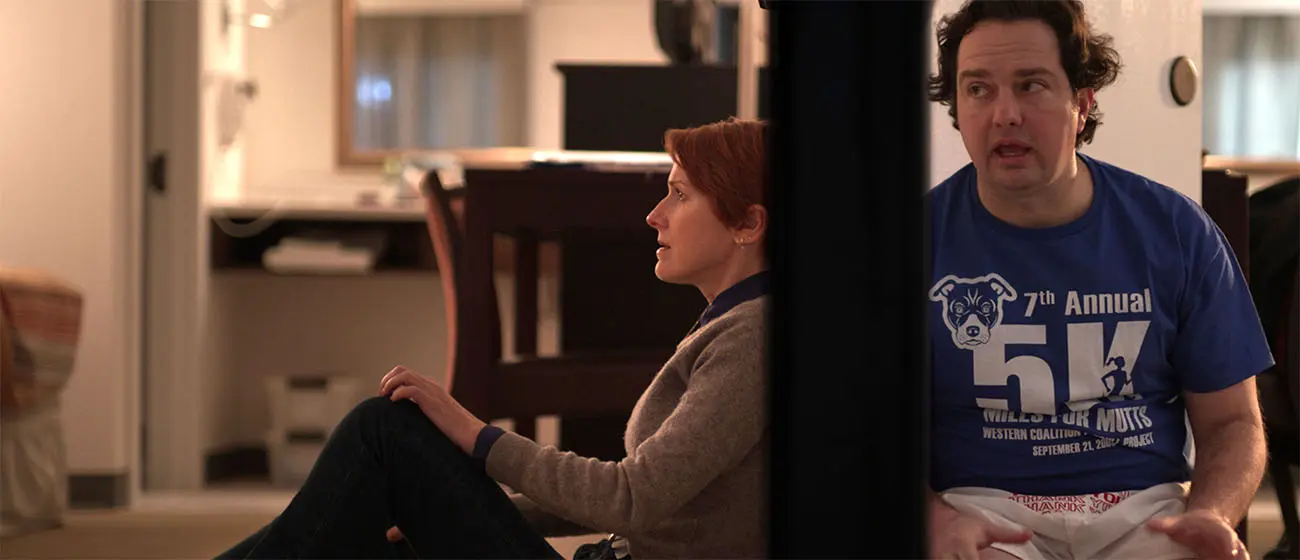 Two people seated on the floor of a living room, separated by a doorway, in a quiet indoor scene.