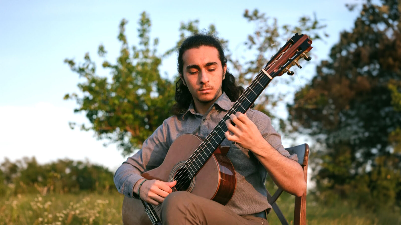 NJIO soloist Baran Güzelsoy playing guitar in the outdoors, under a blue sky