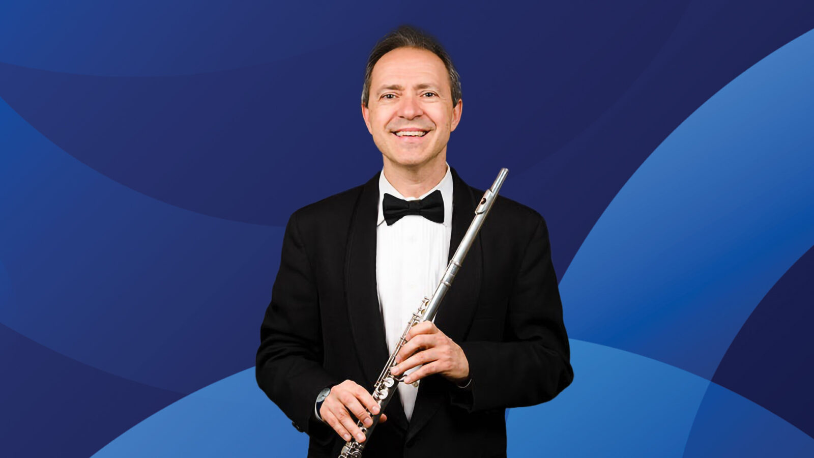 Man in a suit with a flute in hand, smiling. Dark blue background