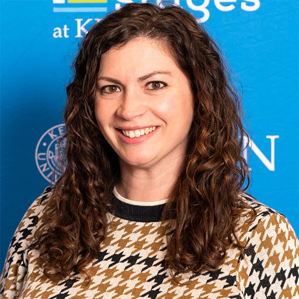 Headshot of a woman with long curly hair, smiling and a checkered shirt