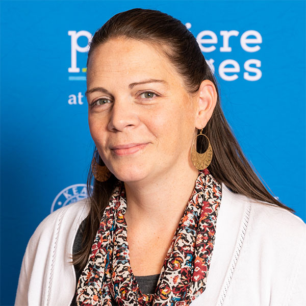 Headshot of a woman wearing a scarf, smiling, with a blue background.