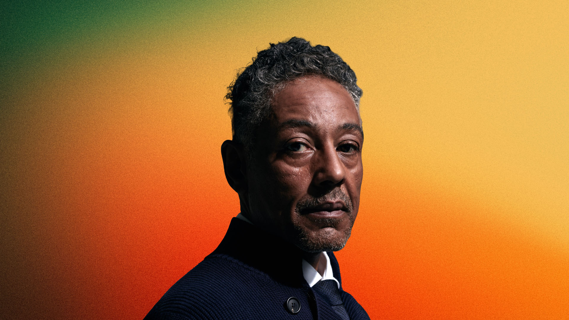 Portrait of Giancarlo Esposito, actor known for his roles in 'Breaking Bad' and 'The Mandalorian,' wearing a dark textured jacket over a white shirt. He has short, curly grey hair and a trimmed goatee, with a contemplative expression as he looks slightly off to the side. The background is a gradient transitioning from green to orange.