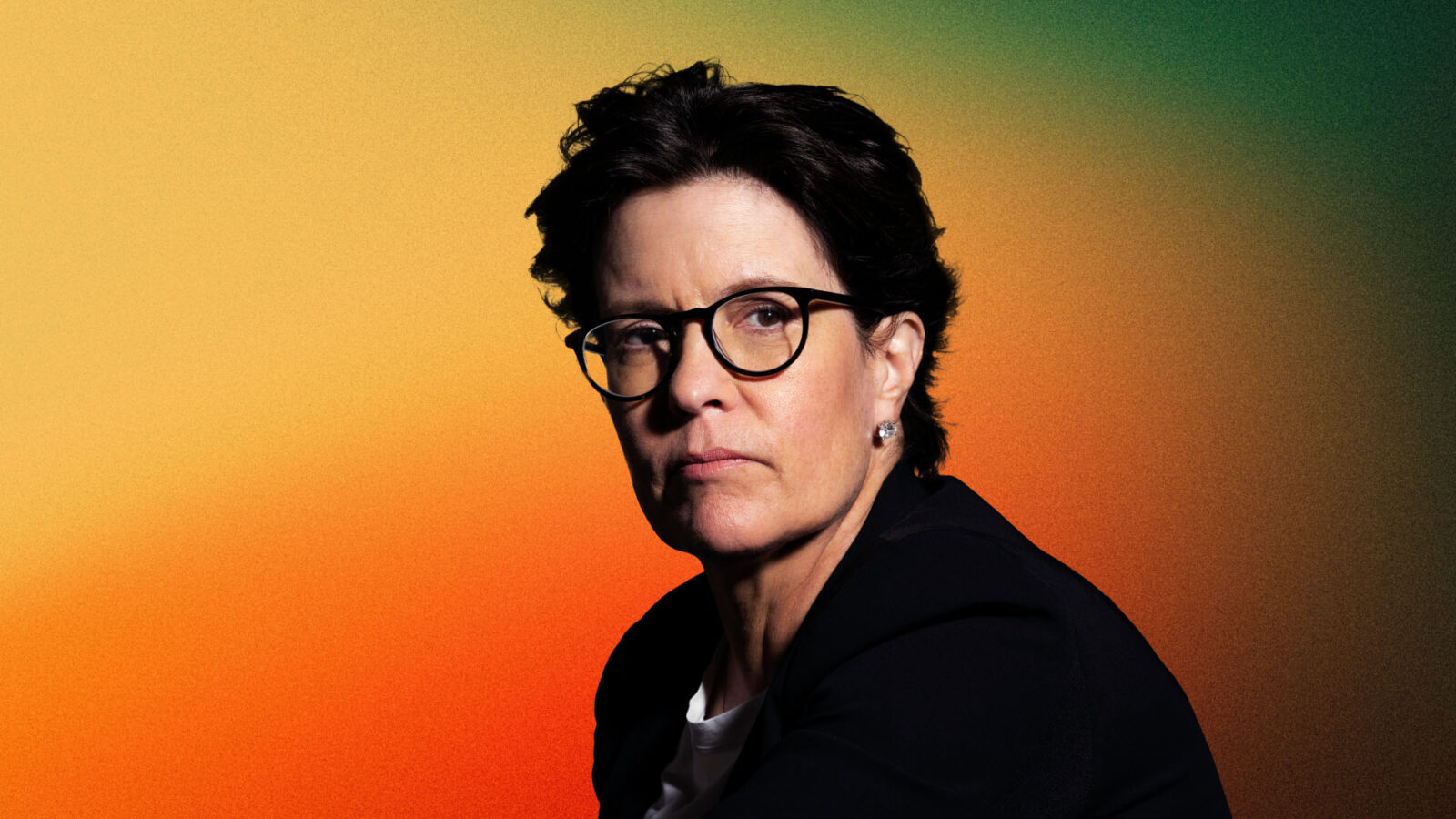 Portrait of Kara Swisher, prominent tech journalist and podcast host, wearing glasses with a dark frame, a black blazer, and a white top. She has short, dark hair and is looking slightly to the side with a serious expression. The background is a gradient transitioning from green to orange.