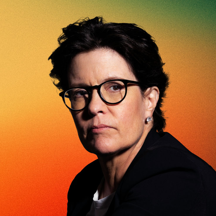 Portrait of Kara Swisher, prominent tech journalist and podcast host, wearing glasses with a dark frame, a black blazer, and a white top. She has short, dark hair and is looking slightly to the side with a serious expression. The background is a gradient transitioning from green to orange.