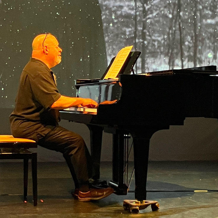 A pianist plays a grand piano on stage, deeply engrossed in his music. The setting features a serene backdrop of a starlit night sky, creating a tranquil and inspiring atmosphere. Sheet music is prominently displayed on the piano, highlighting the performer's dedication to the art of music.