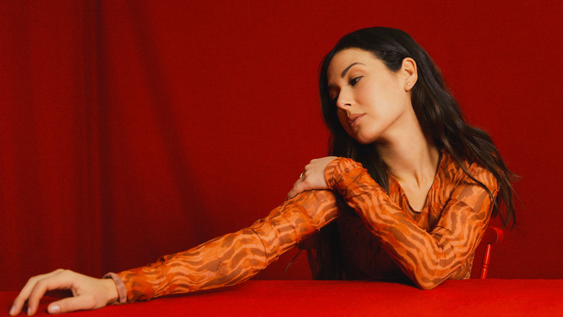 A woman in a red background, looking sideways, dressed in a long sleeve blouse