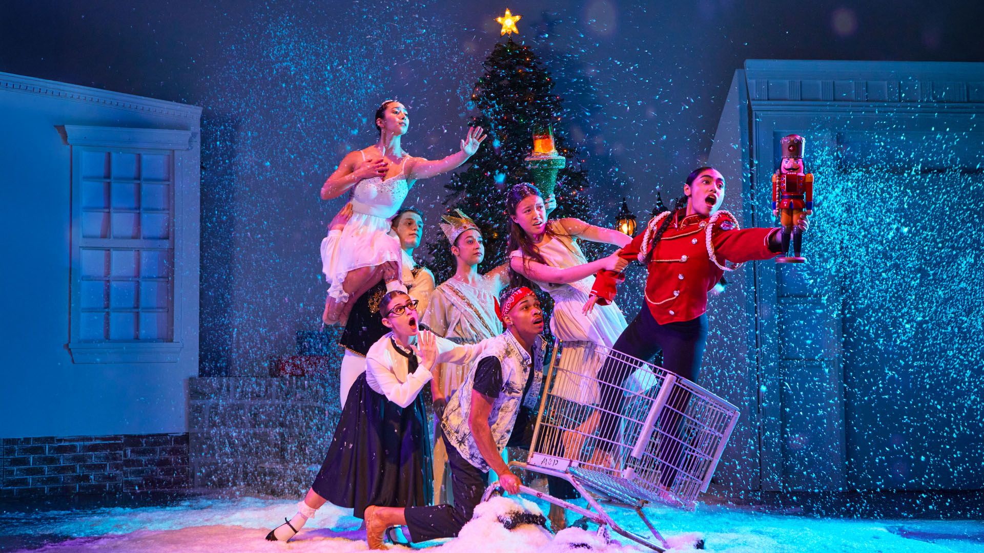 A lively scene featuring a group of dancers in colorful costumes amidst a snowy backdrop, with a decorated Christmas tree and a performer in a toy soldier outfit holding a nutcracker. The energetic composition captures the spirit of a holiday theatrical performance, blending dance and festive elements with a playful and imaginative essence.