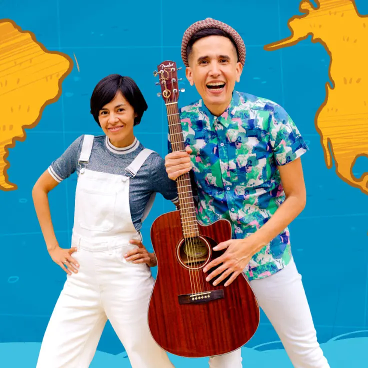 A cheerful duo poses in front of a blue background featuring a map of North and South America. The person on the left wears white overalls and a striped shirt, while the person on the right, holding a guitar, sports a colorful floral shirt and hat.