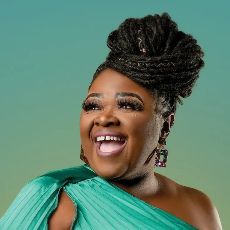 A woman in an exquisite green gown radiates joy and elegance, exuding confidence with a radiant smile. Her intricately styled hair and expressive demeanor reflect grace and poise against a softly hued background.