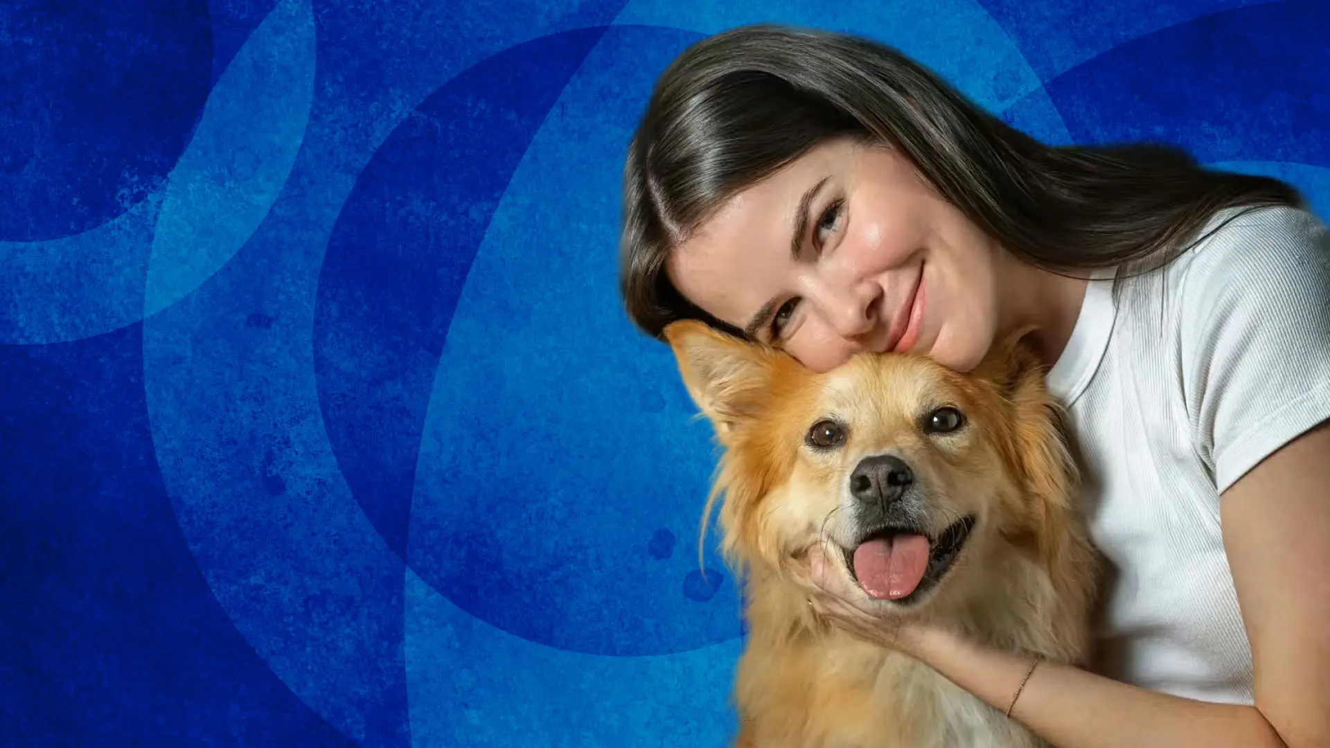 Isabel Klee in a white shirt embracing a fluffy tan dog with perked ears and an open mouth against a blue patterned background.